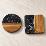 Two decorative coasters with a split black marble and natural wood design, displayed on a light beige marble surface.