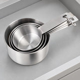 Four stainless steel measuring cups nested together for compact storage.
