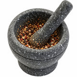 Rounded grinding bowl and matching pestle working against partially crushed spices.