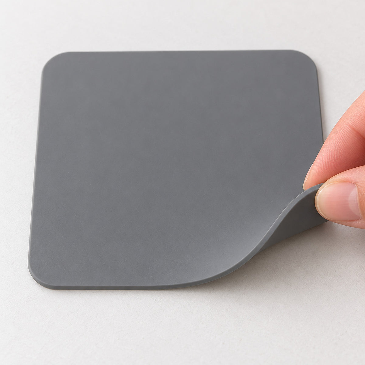 Gray silicone square coaster showing flexibility and thin edge.