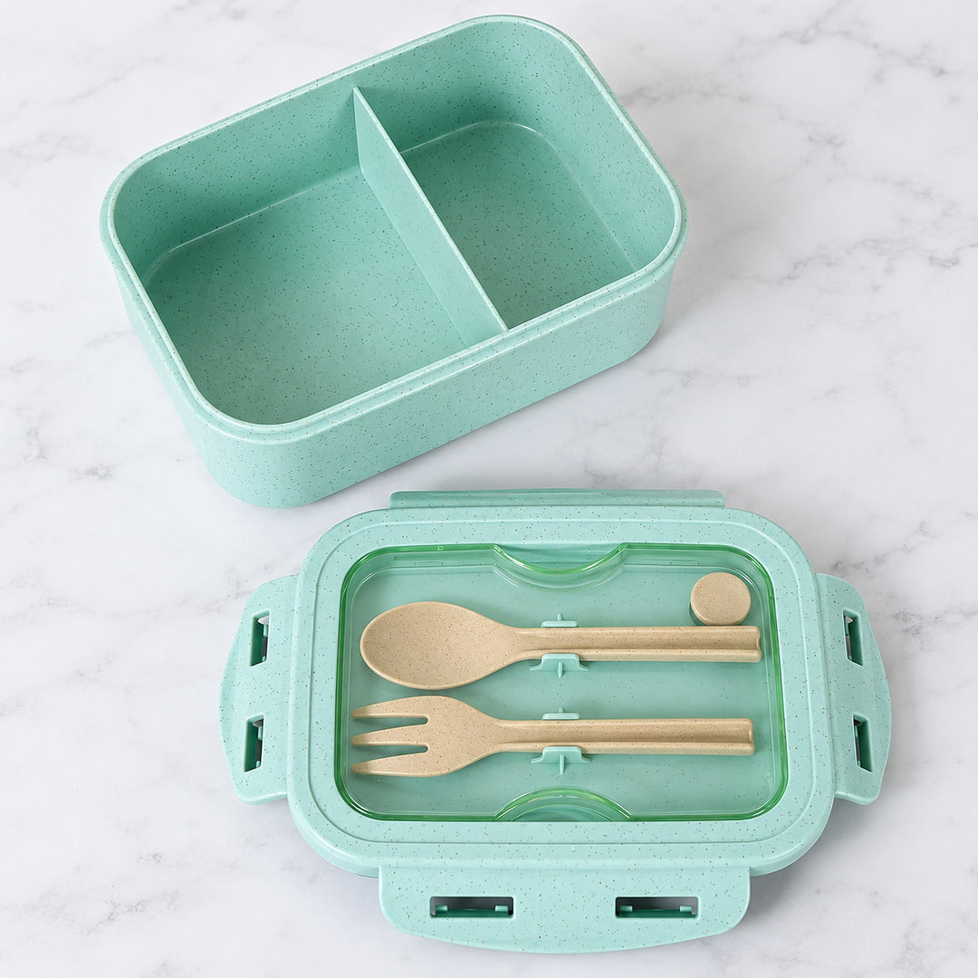 Green lunch box with two compartments and utensils stored beneath clear cover.