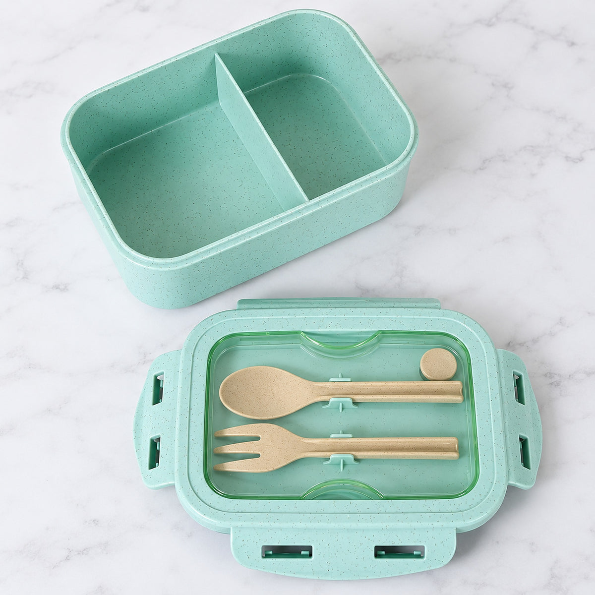 Green lunch box with two compartments and utensils stored beneath clear cover.