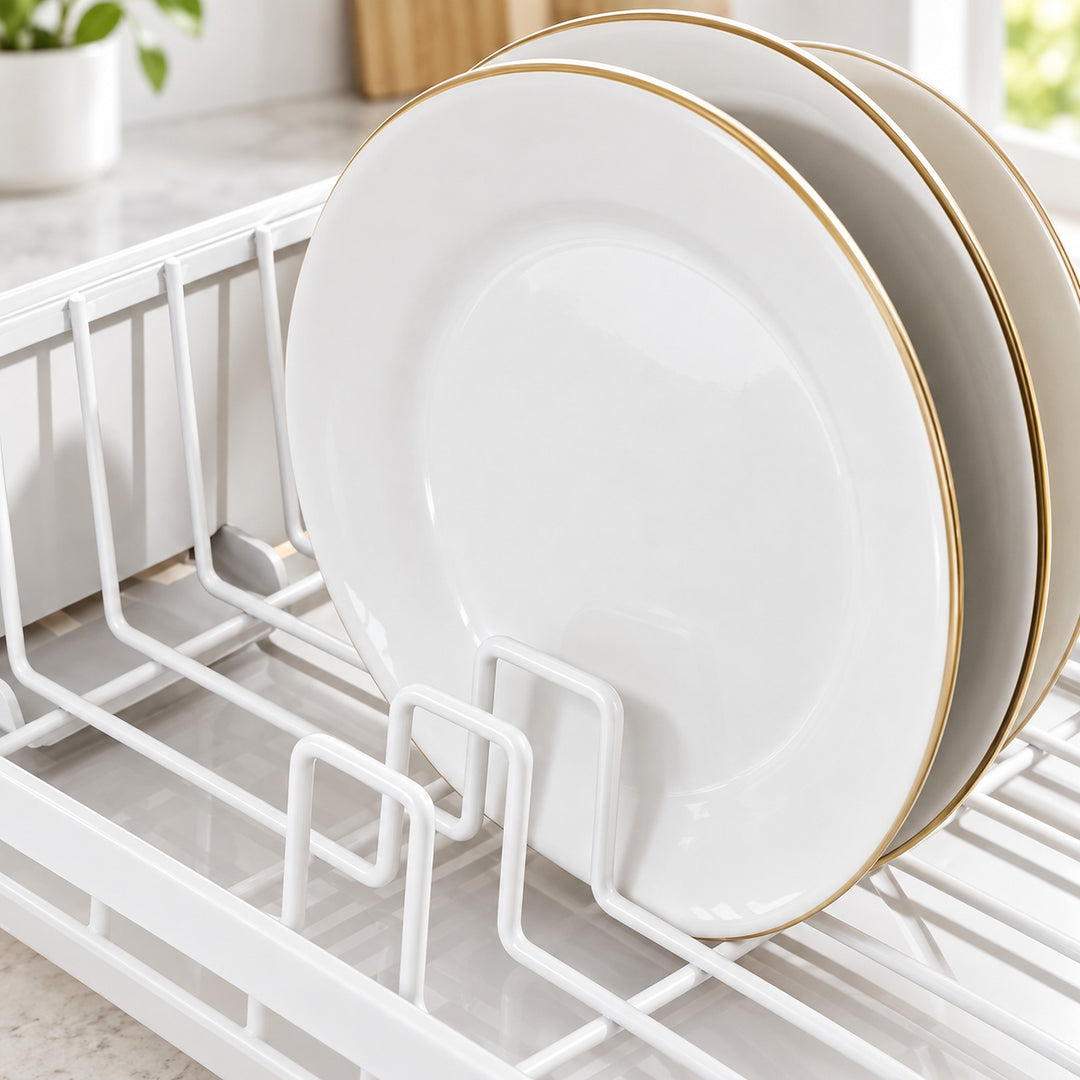 White ceramic plates with gold rims stacked on a white wire dish drying rack in a bright kitchen setting.