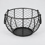 One empty black iron egg basket with two folding handles and a solid circular base.