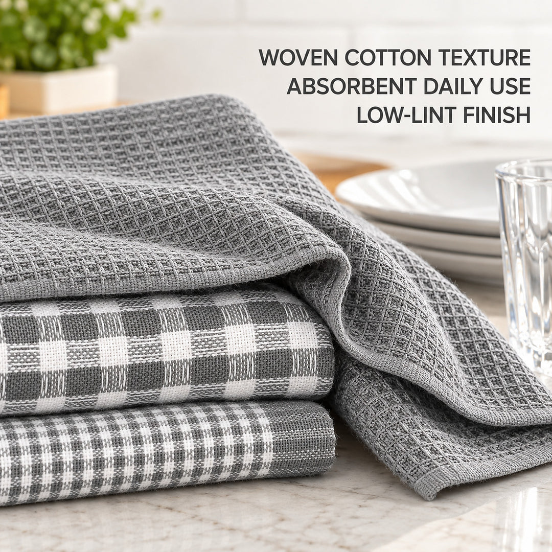 Three folded gray kitchen towels with woven cotton textures, including a plaid pattern, displayed on a marble countertop with a glass and plates in the background. Text on the image reads: 'WOVEN COTTON TEXTURE ABSORBENT DAILY USE LOW-LINT FINISH'.