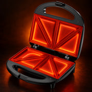 Open black sandwich maker with glowing orange-red heated plates, shown on a dark brown background.