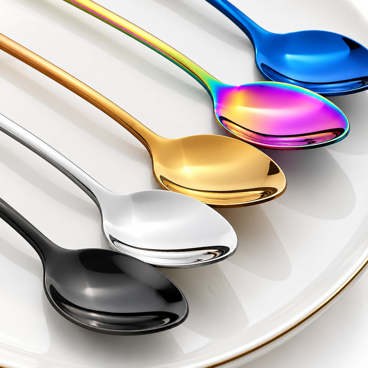 Four stainless steel spoons with different finishes arranged diagonally on a white plate: black, silver, gold, and a rainbow iridescent blue.