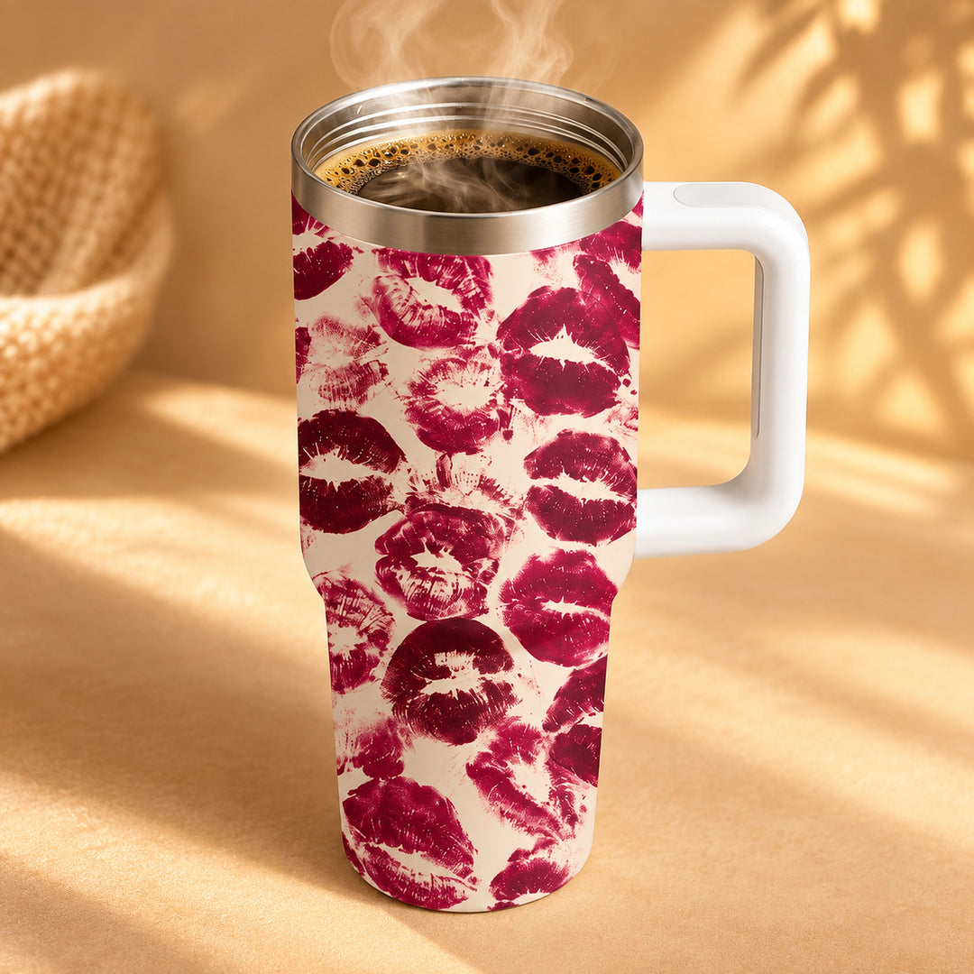 A white handled travel mug filled with a hot beverage, featuring a repeating pattern of dark red lipstick kiss marks on a cream background, set against a warm beige backdrop with soft shadows.