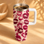 A white handled travel mug filled with a hot beverage, featuring a repeating pattern of dark red lipstick kiss marks on a cream background, set against a warm beige backdrop with soft shadows.