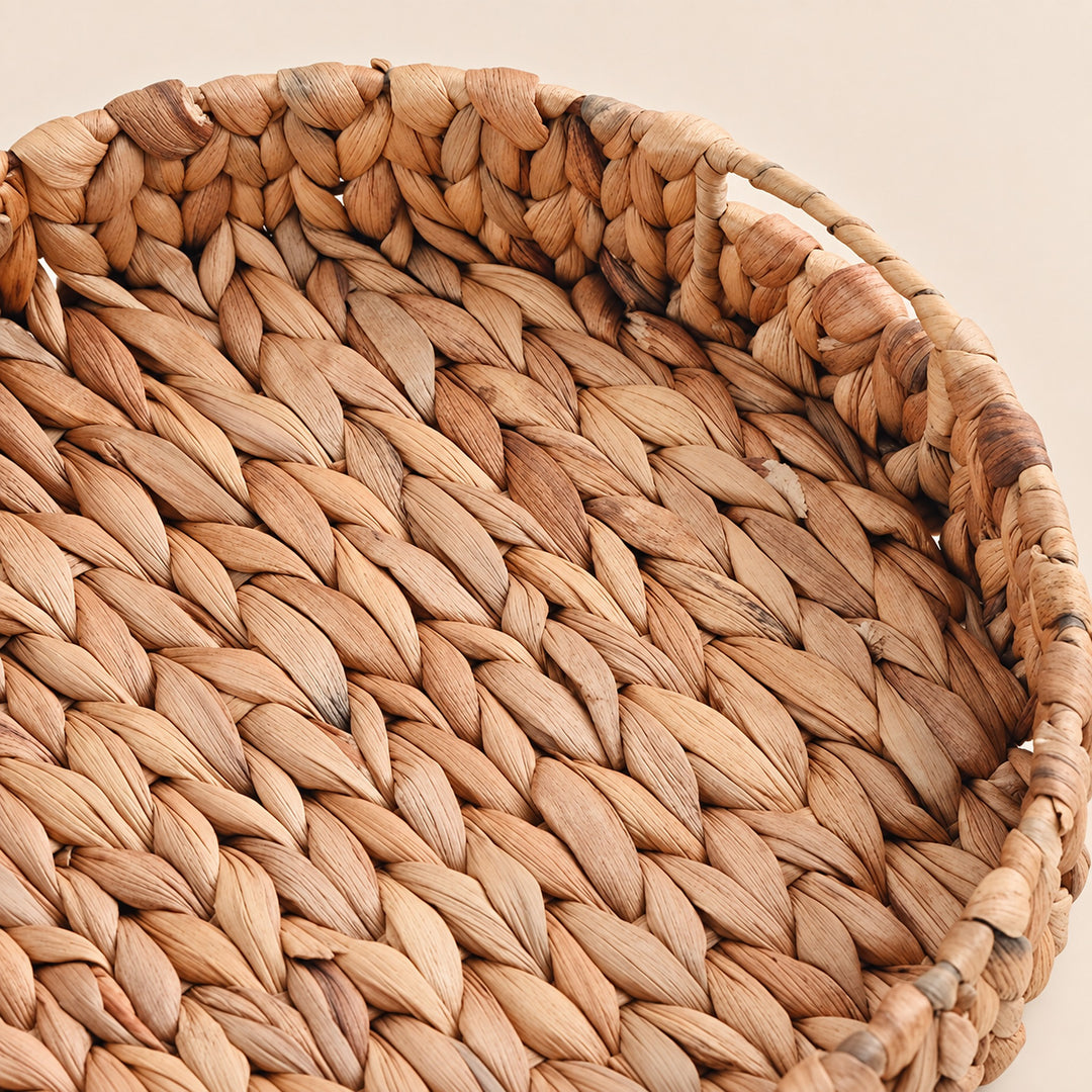 Close-up of a round woven basket made from natural tan and brown seaweed or straw fibers, showing the detailed braided texture and handle on a light beige background.