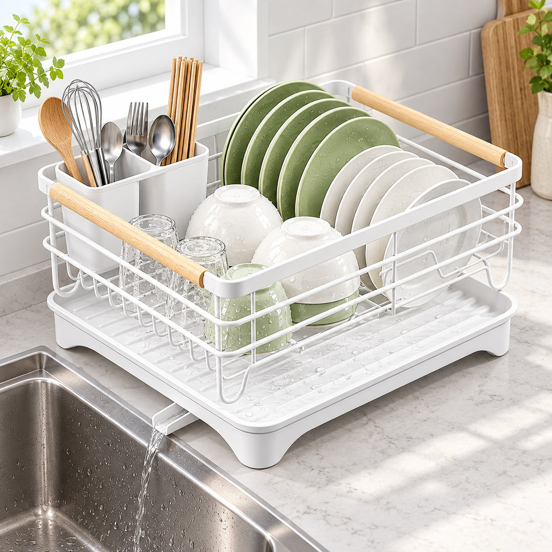 A white plastic and metal dish rack with light wood handles, shown holding green and white plates, bowls, and utensils in a bright kitchen setting above a sink.