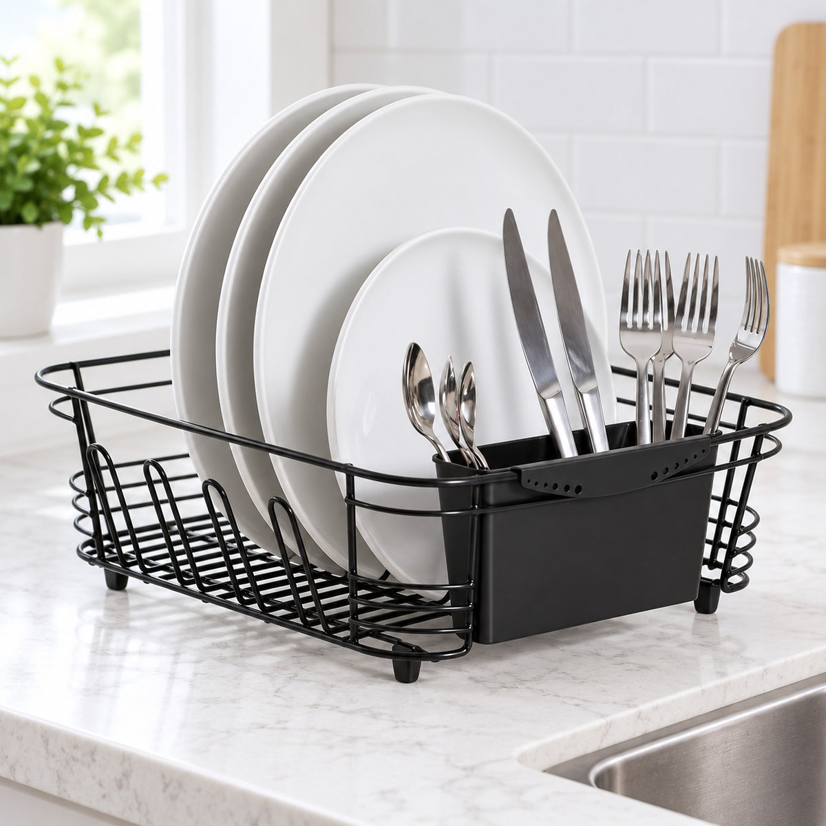 A black wire dish drying rack with a matching black utensil holder, shown on a kitchen counter with white plates and silver cutlery inside. The background features a white subway tile wall and a window.