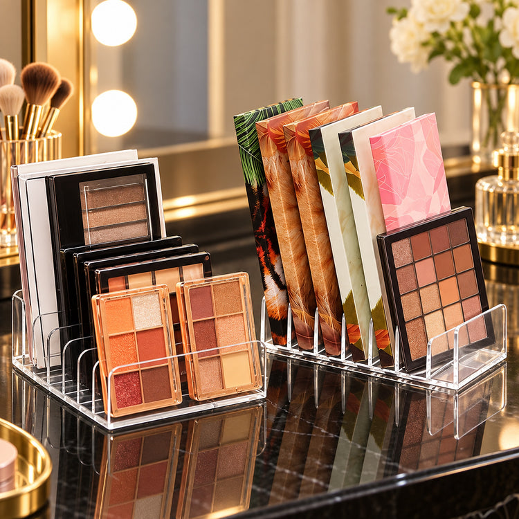 Clear acrylic makeup organizer stands on a glossy black marble vanity surface, holding eyeshadow palettes and colorful makeup booklets in a bright vanity setting with mirror lights and flowers in the background.