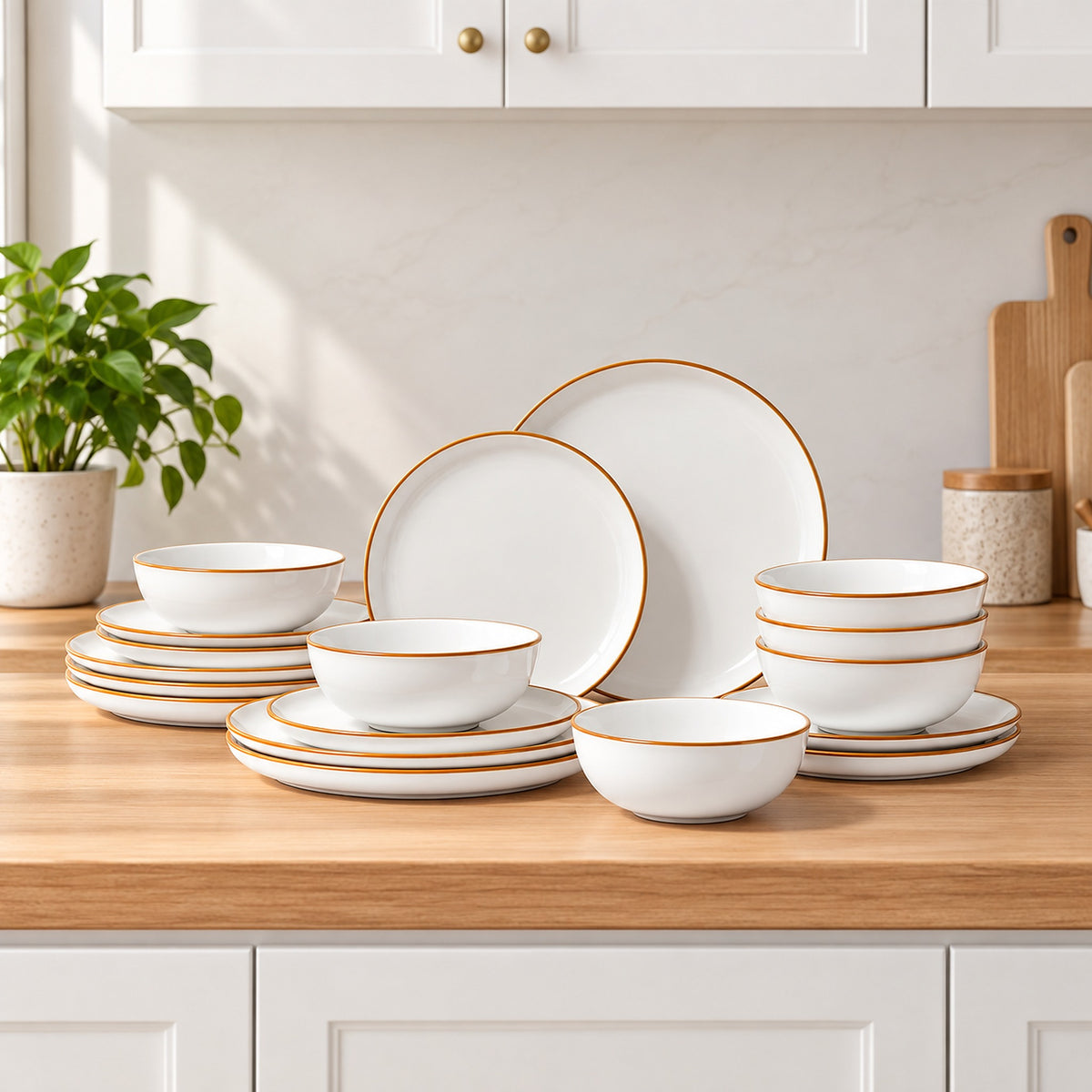 A coordinated dinnerware set arranged on a wooden kitchen counter, including white plates and bowls with thin gold rims. White cabinets, a potted plant, and kitchen accessories are visible in the background.