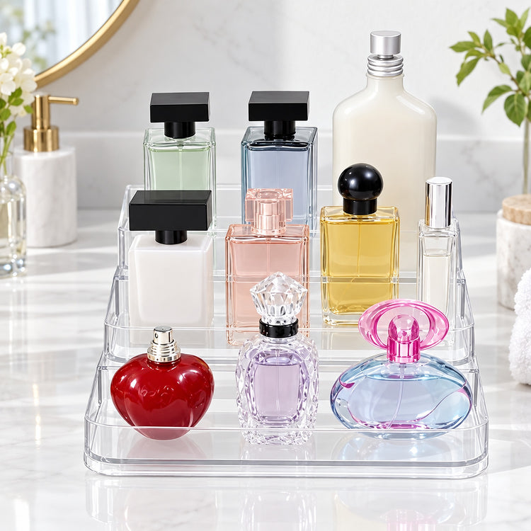 A clear acrylic perfume organizer tray holding multiple decorative perfume bottles in assorted colors, set on a white marble countertop with bathroom decor in the background.