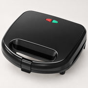 A black electric sandwich maker or mini toaster with a carrying handle, featuring red and green power buttons on top, shown on a light gray background.
