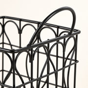 Close-up of a black metal wire basket with a curved top handle and decorative arched wire patterns, shown against a plain light background.