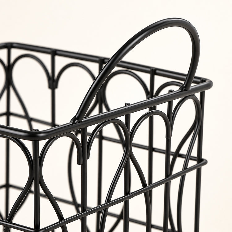 Close-up of a black metal wire basket with a curved top handle and decorative arched wire patterns, shown against a plain light background.