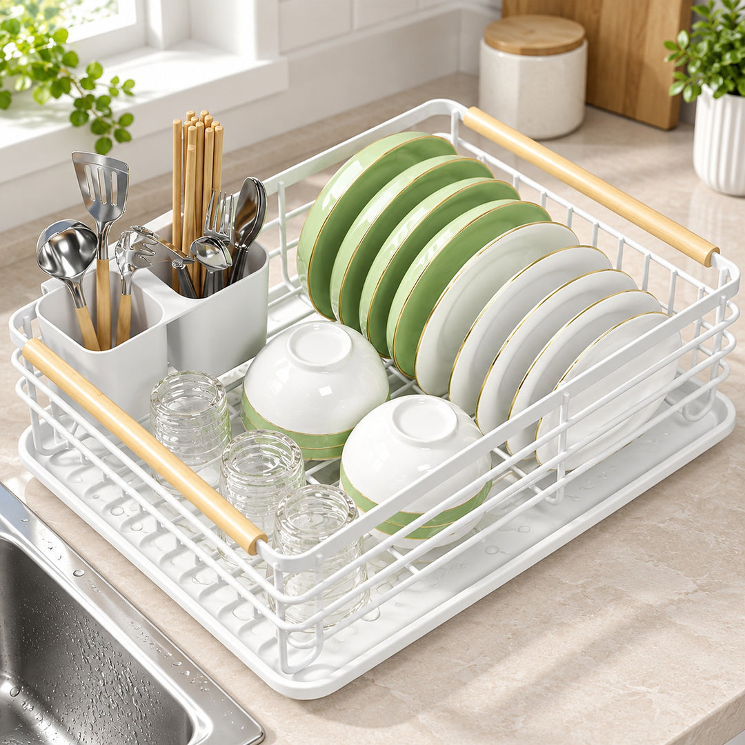 A white plastic and metal dish drying rack with light wood handles, shown in a kitchen setting with green and white plates, bowls, and utensils inside.