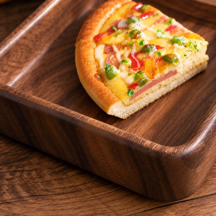 A triangular slice of gourmet pizza with a thick golden crust, topped with melted cheese, green olives, red peppers, and ham, served on a dark wooden square tray.