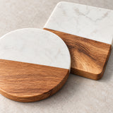 Two half-marble and half-wood coasters on a light beige stone surface. One coaster is round and the other is square, both featuring a white marble top half and a warm medium-brown wood bottom half.