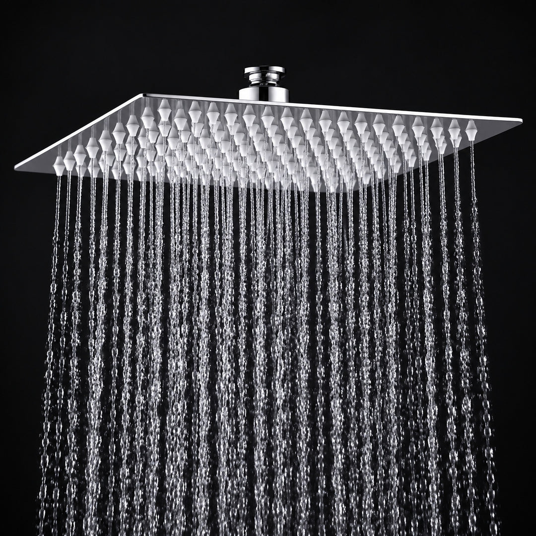 A square rain shower head with a textured chrome finish, shown with water droplets falling from its multiple nozzles against a solid black background.
