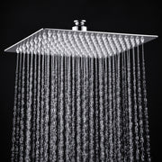 A square rain shower head with a textured chrome finish, shown with water droplets falling from its multiple nozzles against a solid black background.