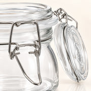 Clear glass jar with a silver metal clamp lid and glass seal, shown close up on a light beige background.