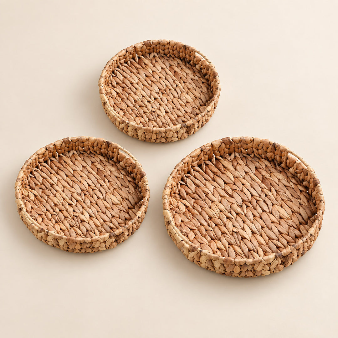 Three round woven natural fiber trays in different sizes arranged on a light beige background.