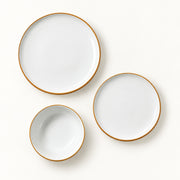 Three-piece white ceramic dinnerware set with a thin gold rim, including a large plate, a medium plate, and a small bowl, arranged on a clean white background.