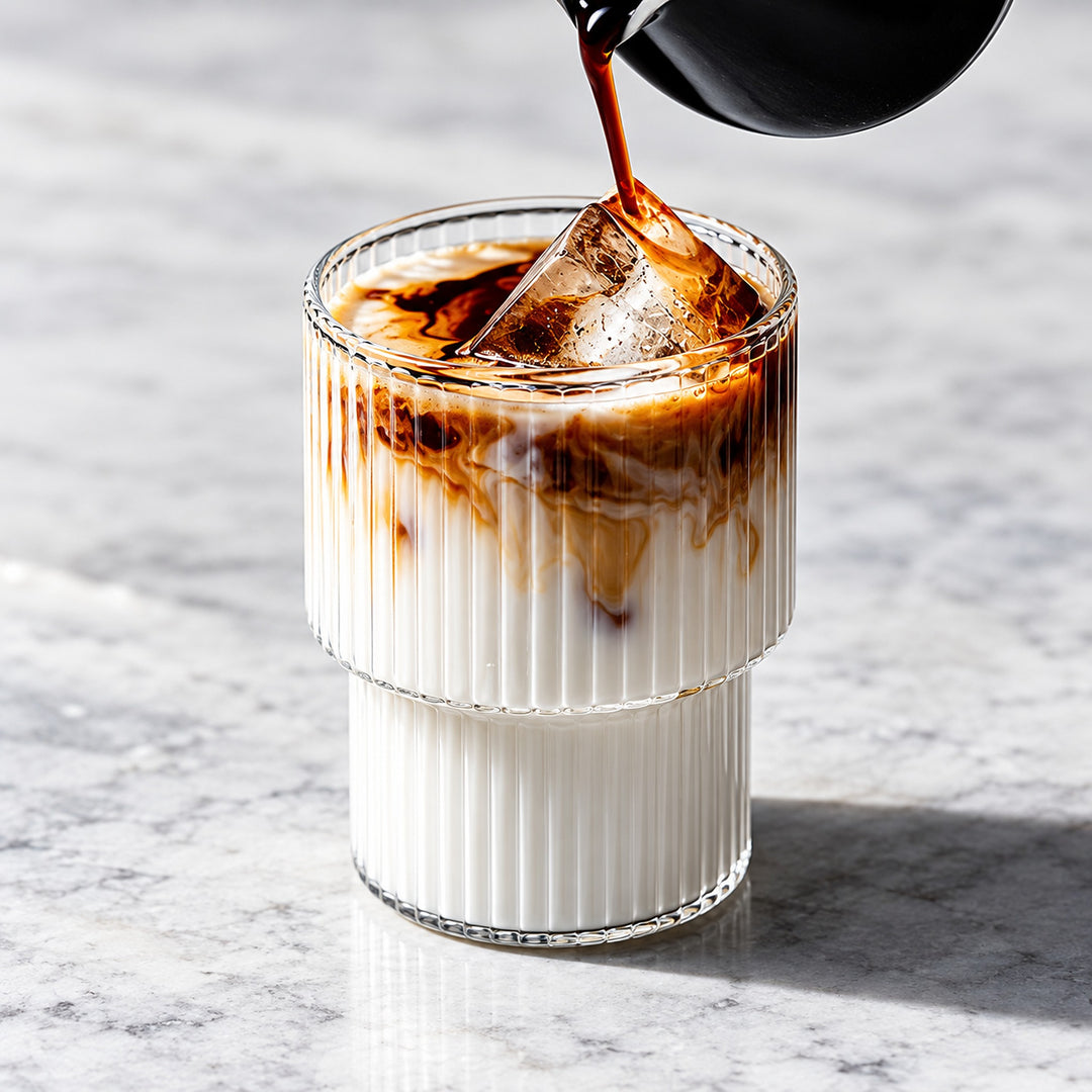 Iced coffee poured into one clear ribbed stepped-base glass.