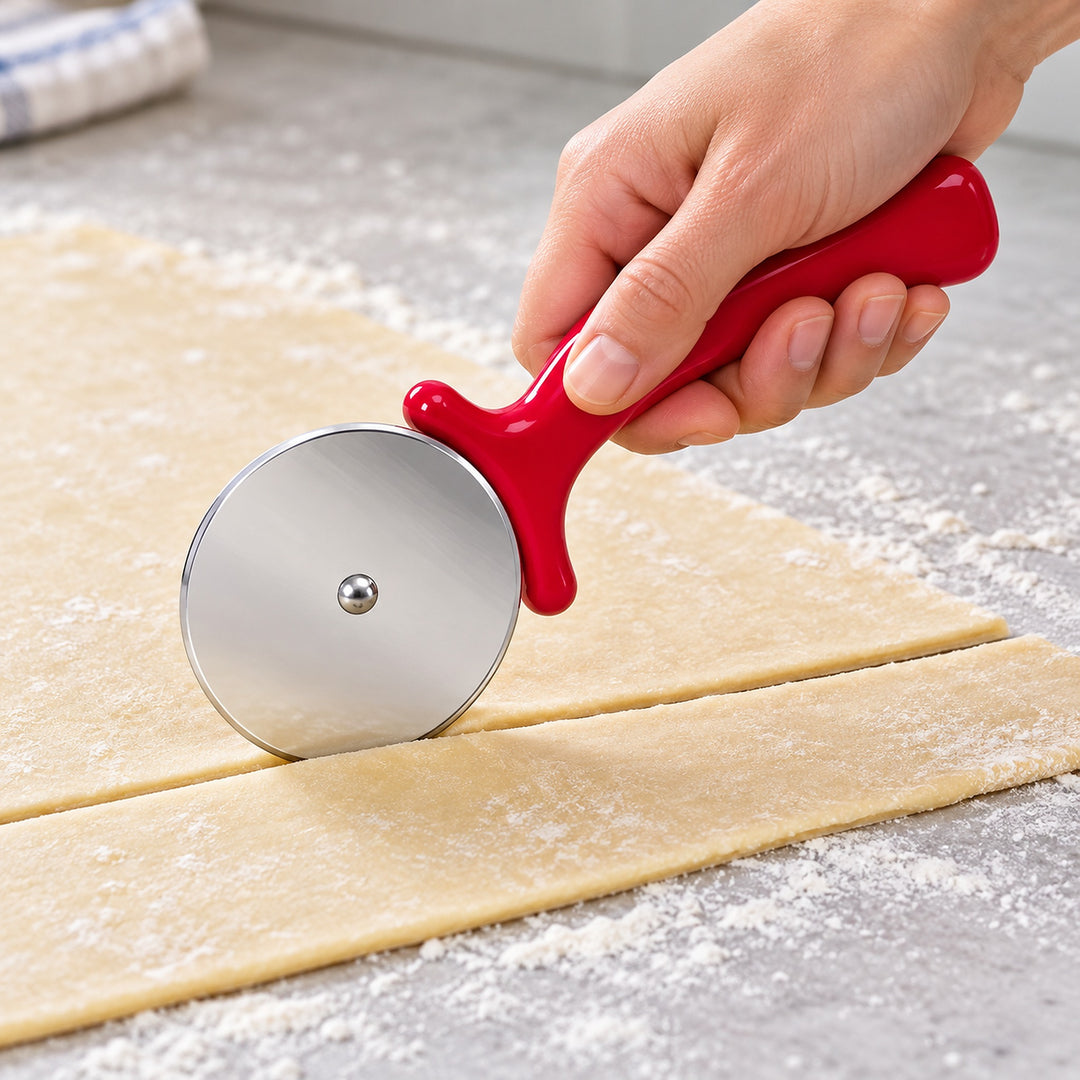 Red handled pizza wheel cutting a strip of pastry dough.