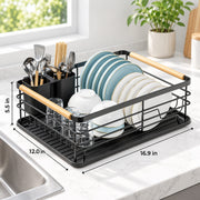 Black wire dish rack with light wood handles on a white marble kitchen counter, shown holding plates, bowls, glasses, and utensils. Dimension labels 12.