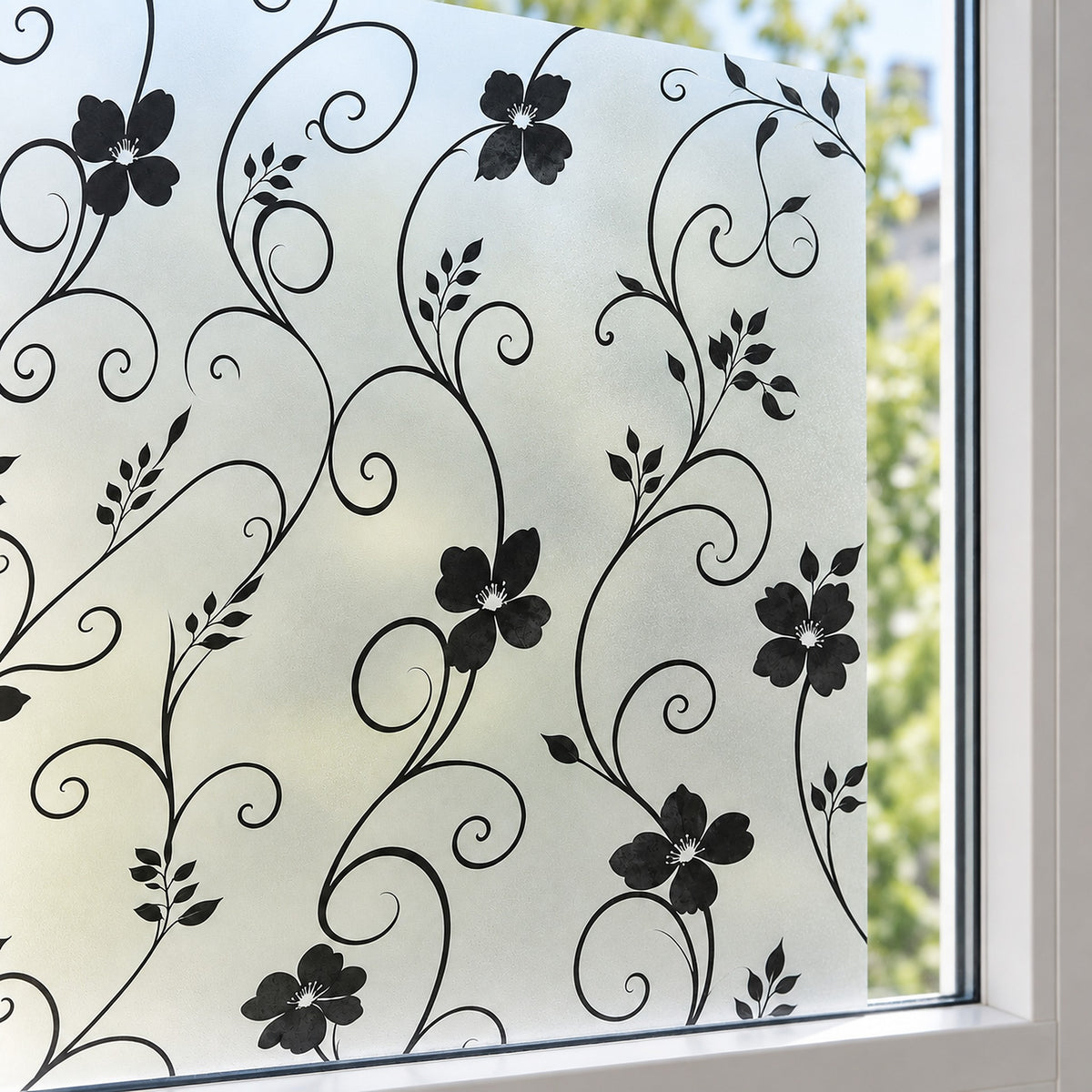 Black floral and scroll vine window film applied to a frosted glass window pane, with a white window frame and blurred green outdoor foliage visible in the background.