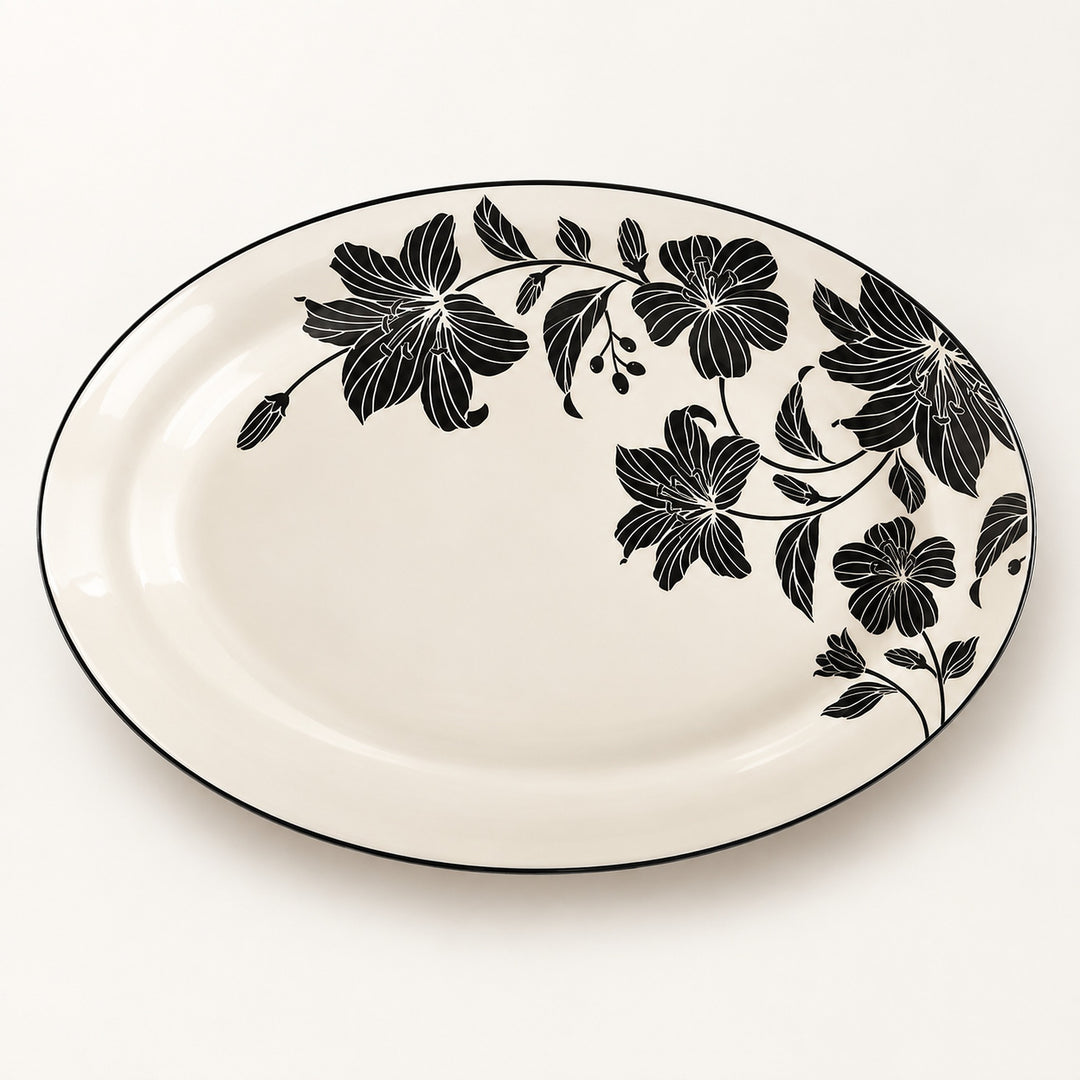 An oval ceramic serving platter with a glossy white background and a black floral vine pattern along the right side and rim, set against a clean white background.