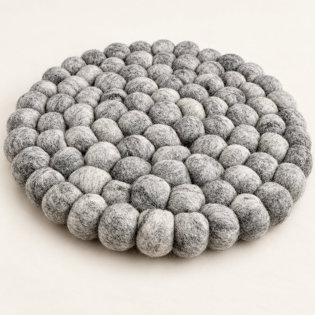 A round, low-profile floor cushion made of dense, textured gray felt pom-poms, photographed on a clean, solid off-white background.