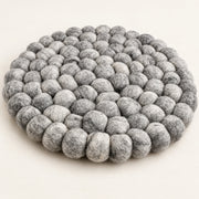 A round, low-profile floor cushion made of dense, textured gray felt pom-poms, photographed on a clean, solid off-white background.