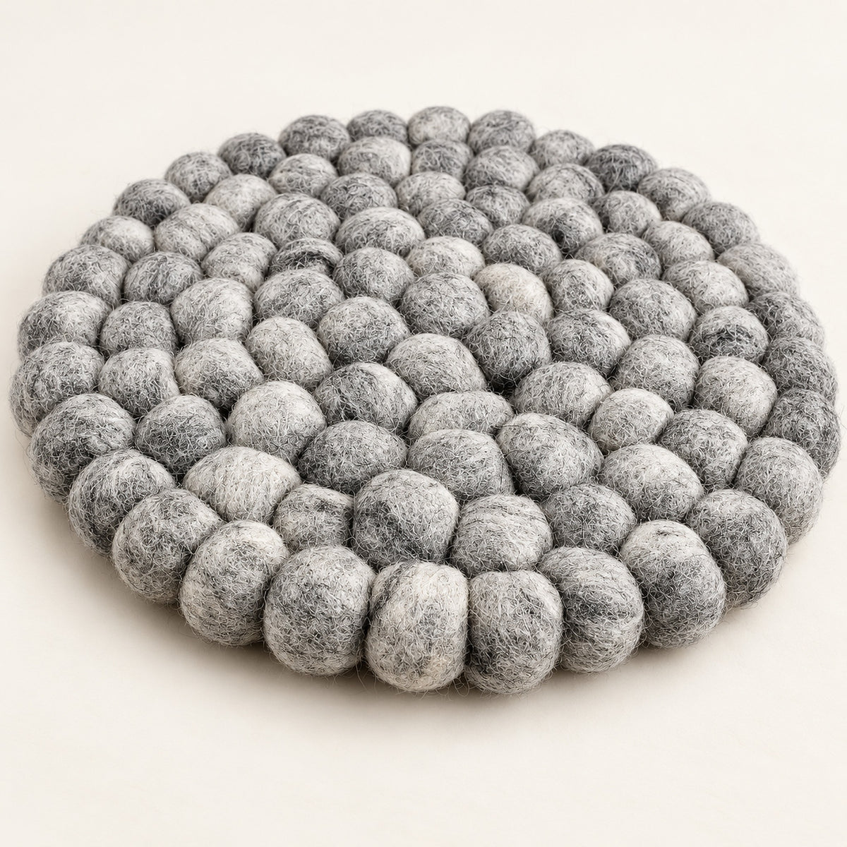 A round, low-profile floor cushion made of dense, textured gray felt pom-poms, photographed on a clean, solid off-white background.