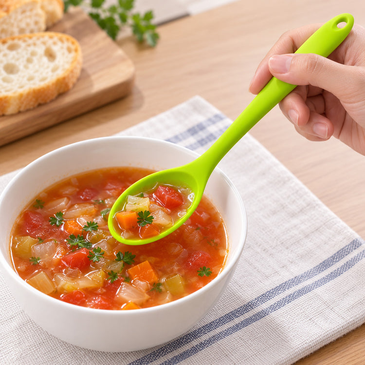 Lime-green silicone spoon serving tomato vegetable soup.