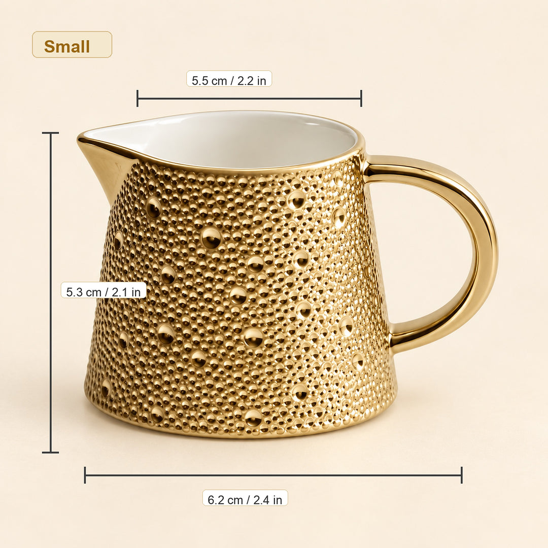 A small gold ceramic pitcher with a textured, bubble-like perforated pattern and a curved handle, shown with dimension lines and labels indicating its height, width, and spout width on a light beige background.