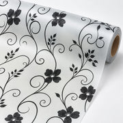 A roll of white wallpaper featuring a black floral and vine pattern, shown partially unrolled on a clean white background.