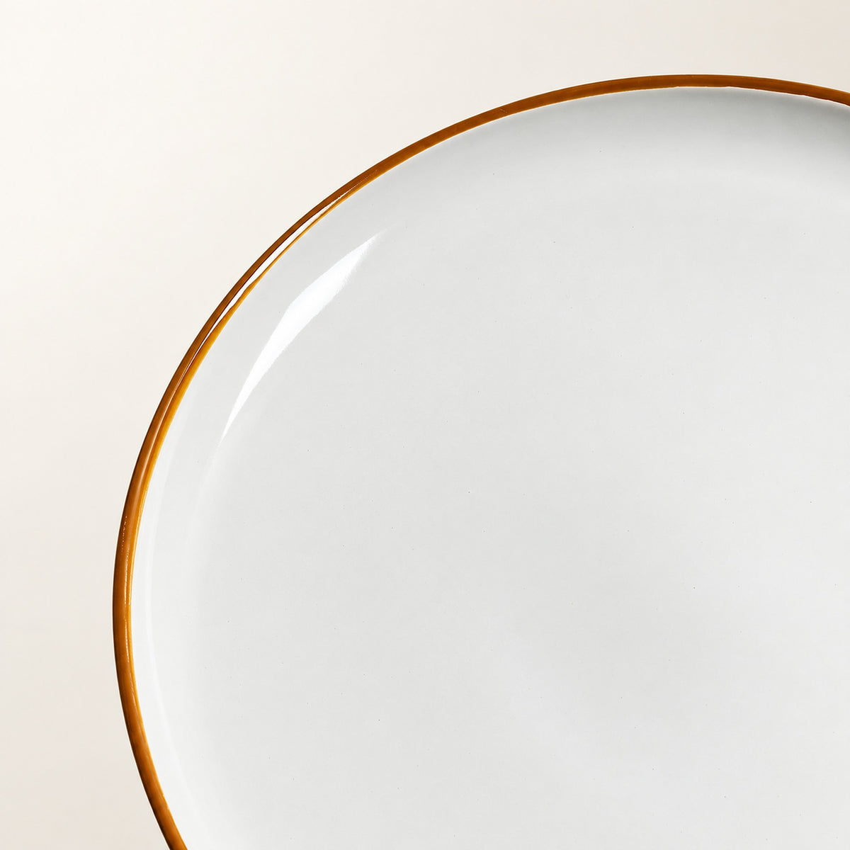 Close-up of a white ceramic plate with a thin warm brown rim, photographed against a light beige background.