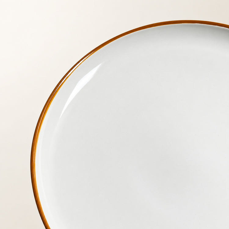 Close-up of a white ceramic plate with a thin warm brown rim, photographed against a light beige background.