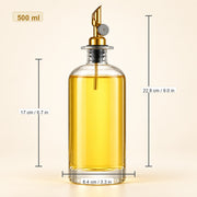 A 500 ml clear glass oil dispenser bottle filled with golden yellow oil, featuring a gold-toned metal pour spout and black collar. The image includes dimension lines and text showing the bottle's height (22.