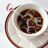 Pink heart glass stirrer in iced coffee viewed from above.