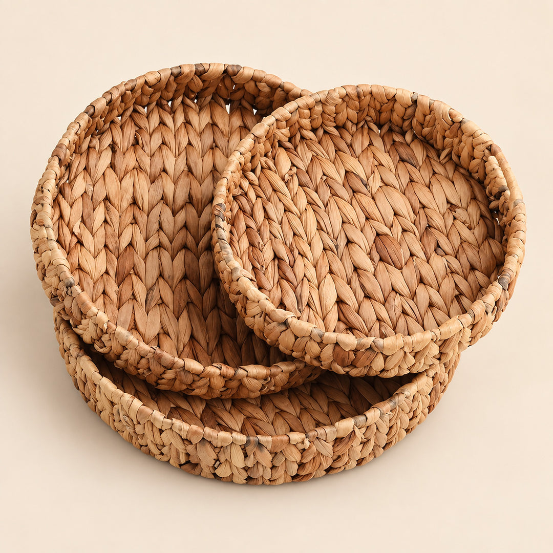 Three round woven seagrass or straw baskets in nested sizes, displayed on a solid light beige background.