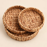 Three round woven seagrass or straw baskets in nested sizes, displayed on a solid light beige background.