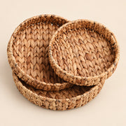 Three round woven seagrass or straw baskets in nested sizes, displayed on a solid light beige background.