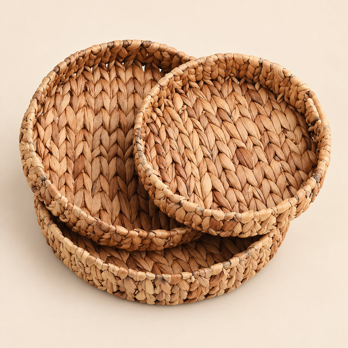 Three round woven seagrass or straw baskets in nested sizes, displayed on a solid light beige background.
