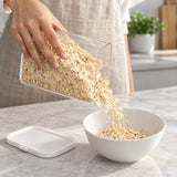 Pouring oats from a clear storage container into a breakfast bowl.